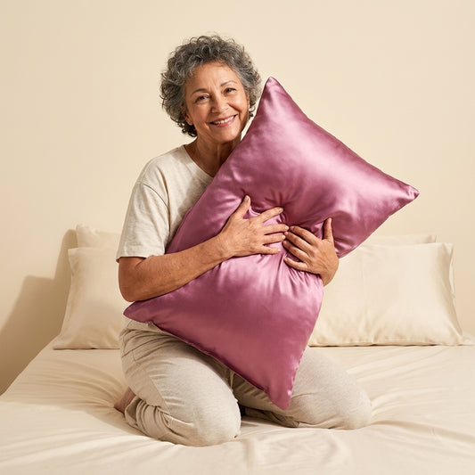 Taie d'oreiller en soie de mûrier Novani, coloris vieux rose, tenue contre soi sur un lit